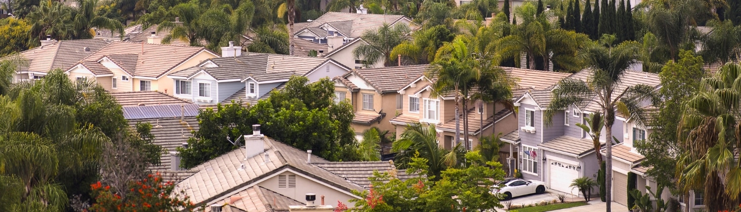 Aerial view of a suburban neighborhood showing rows of houses with varying roof designs built by Bonita ADU builders, surrounded by lush greenery.